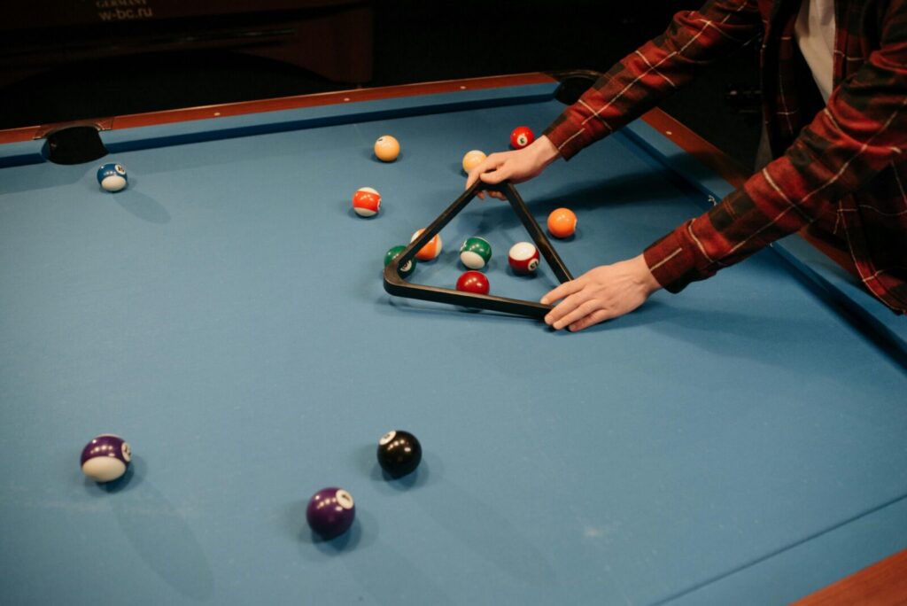 A person arranging billiard balls on a blue pool table in preparation for a game indoors.